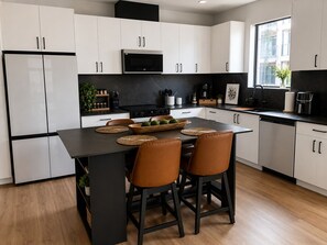 A modern kitchen with white cabinets, a black countertop, and a central island with stools. - Brand new 2-bedroom condo in beautiful New Braunfels (New Braunfels)