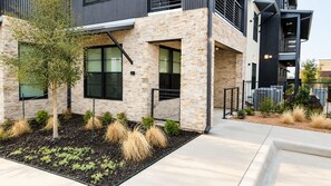 A modern building with a stone facade, large windows, and a landscaped area with plants and a tree. - Brand new 2-bedroom condo in beautiful New Braunfels (New Braunfels)