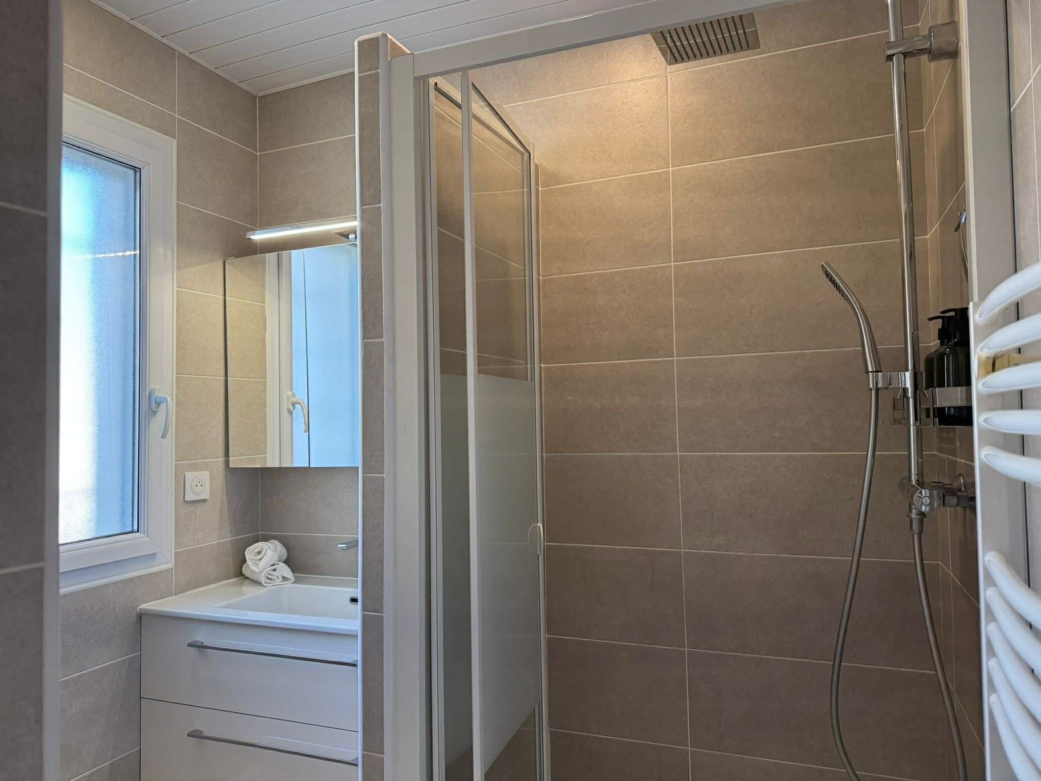 Une salle de bain avec une douche, un lavabo, un miroir et une fenêtre.