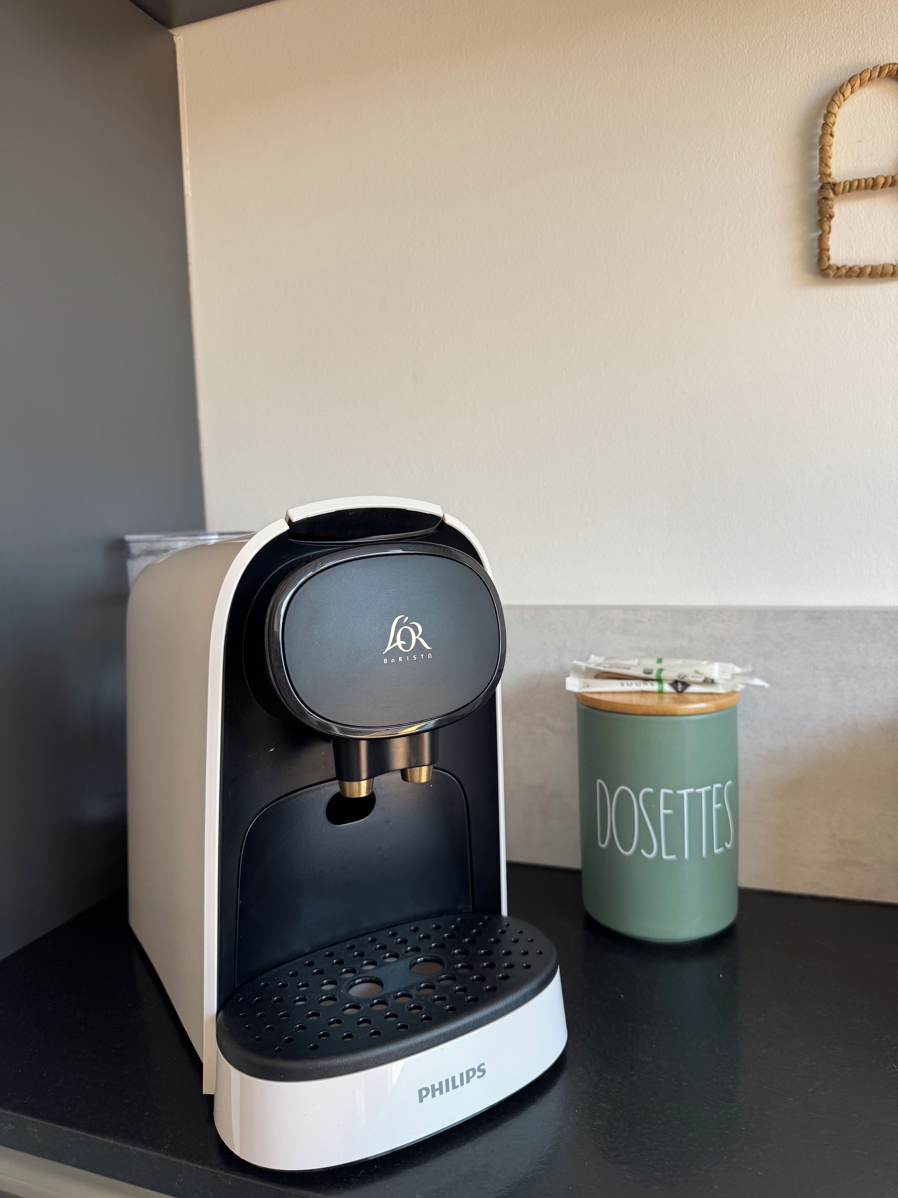 A coffee maker with a logo, a green container with 'DOSETTES' text, and a black countertop.