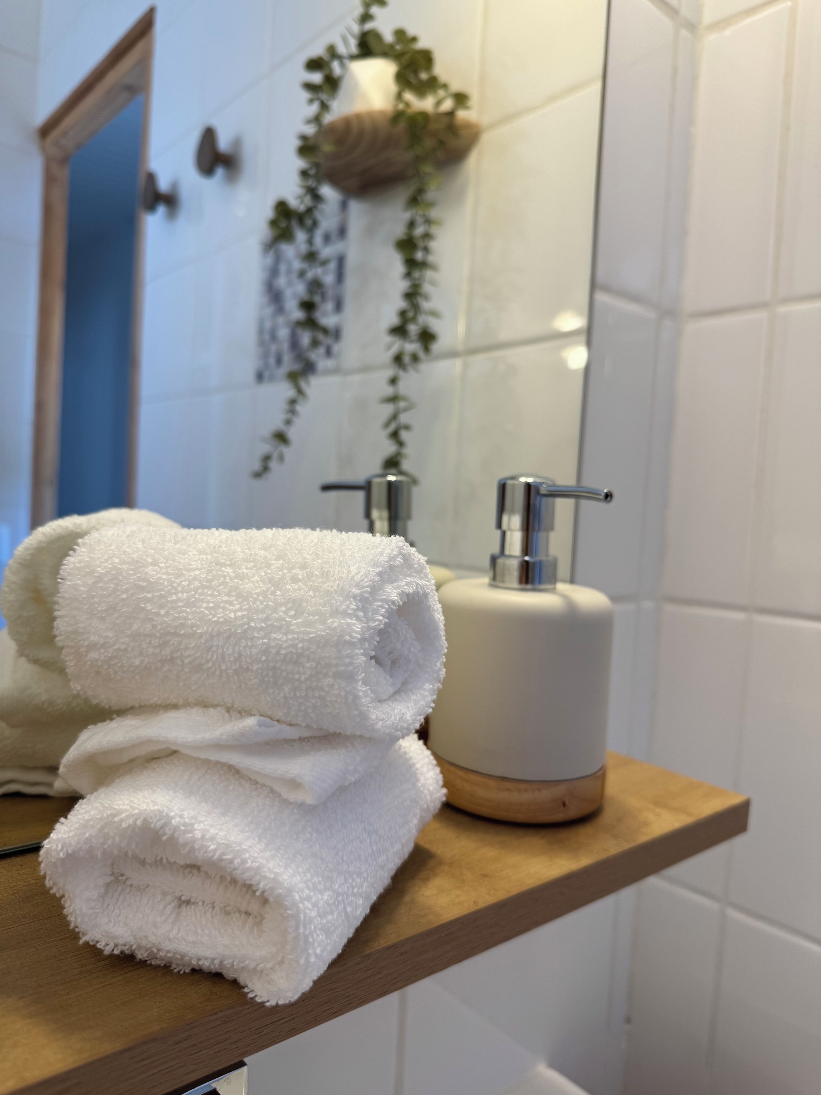 Een badkamer met een houten plank met opgevouwen handdoeken en een witte zeepdispenser.