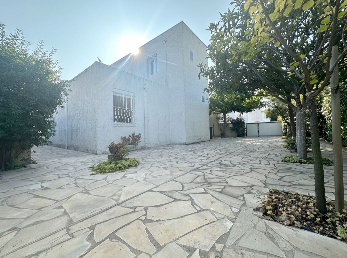 A building with a stone-paved courtyard, a window with bars, and a tree with yellow flowers.