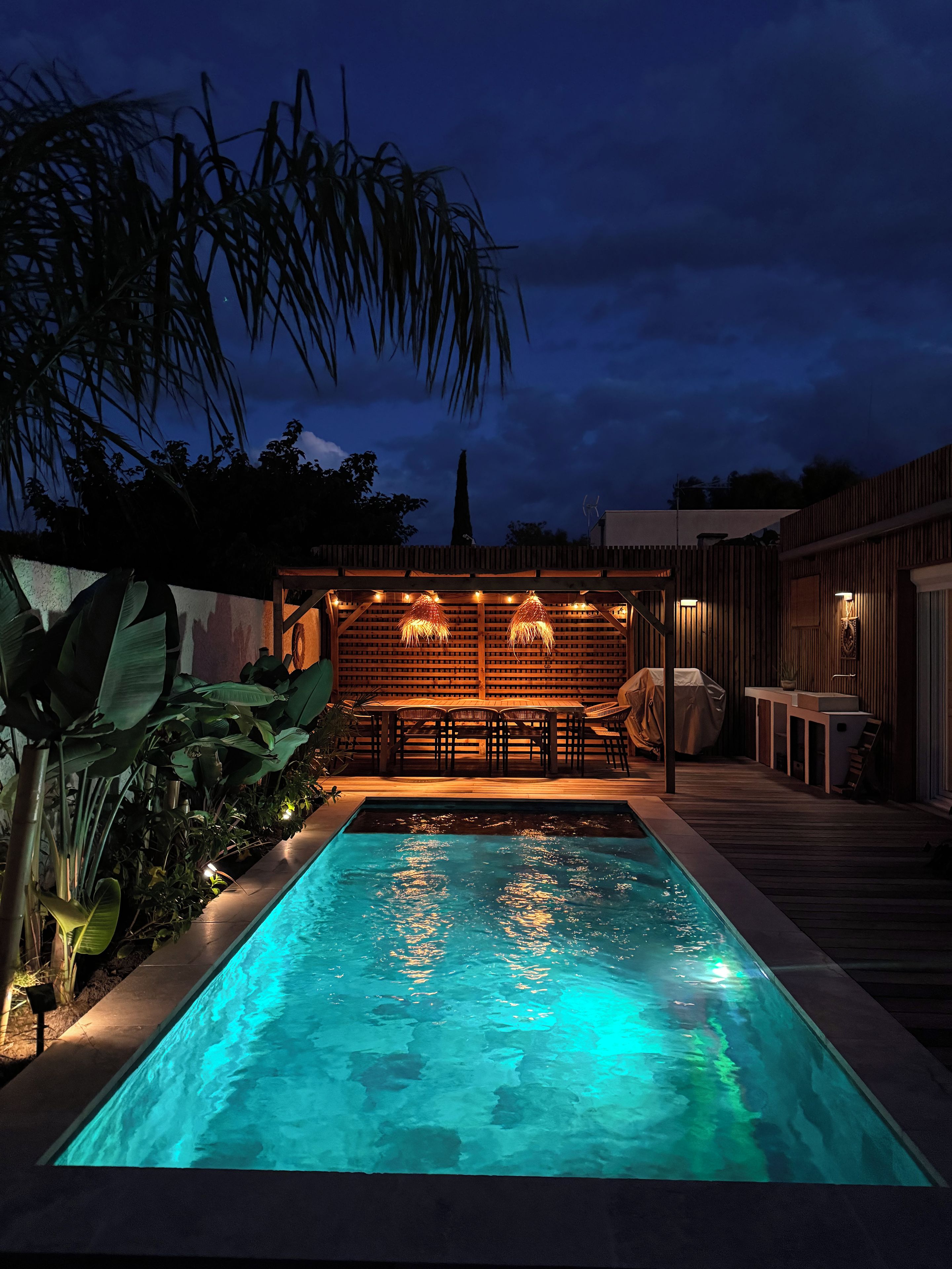 A swimming pool with a wooden deck and a covered seating area with tables and chairs.