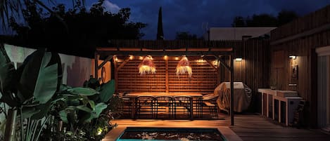 A swimming pool with a wooden deck and a covered seating area with tables and chairs.