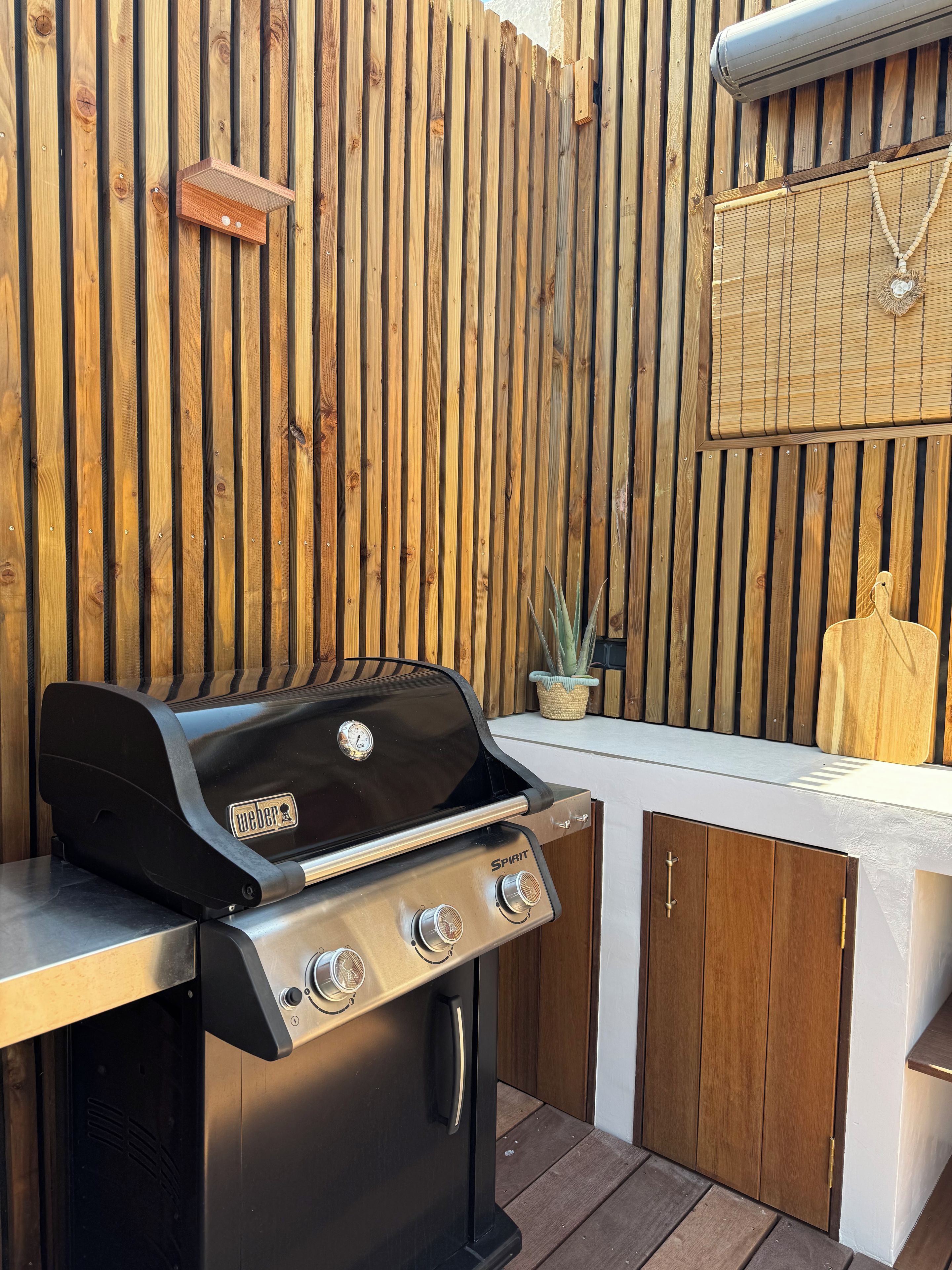 A barbecue grill with a control panel, a wooden fence, and a small potted plant.