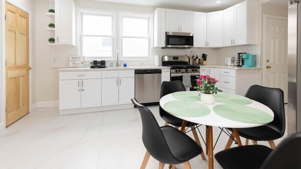 Une cuisine moderne avec des armoires blanches, un four à micro-ondes en acier inoxydable, une cuisinière et un lave-vaisselle. On y trouve une table à manger avec des chaises noires et un vase rempli de fleurs.