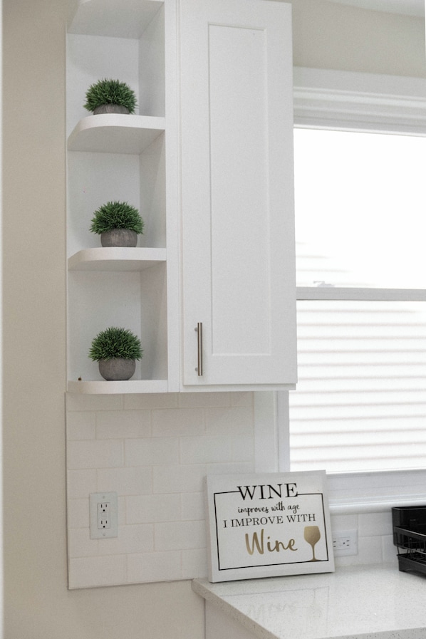 A kitchen with white cabinetry, three potted plants on shelves, and a sign on the wall.