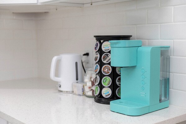 Una cocina con cafetera, balanza y un tarro de cápsulas de café sobre la encimera.