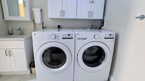 Une buanderie équipée de deux machines à laver LG blanches, d’un évier blanc et de placards.