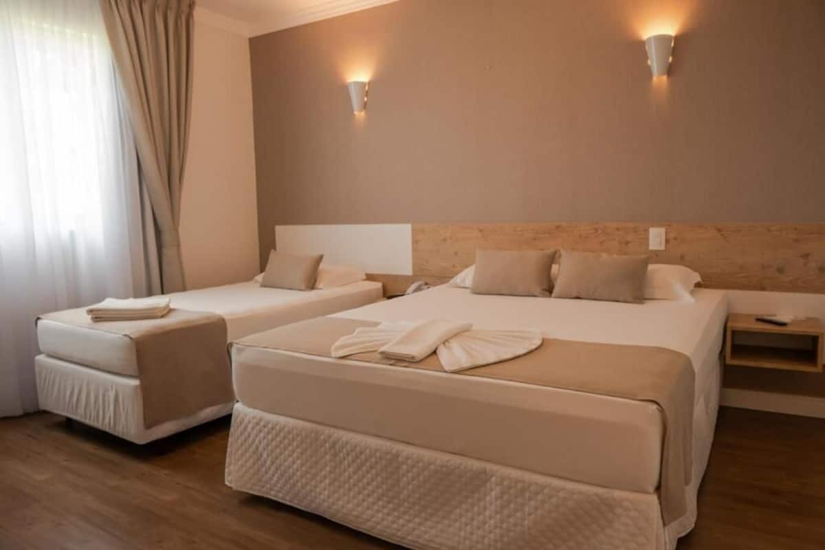 A hotel room with two beds, a wooden headboard, bedside tables, and wall-mounted lights.