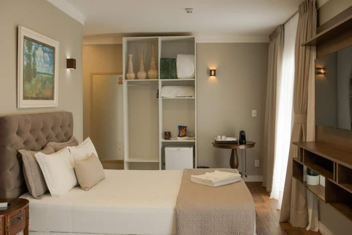 A hotel room with a large bed, a wardrobe, a small table, and a painting on the wall.