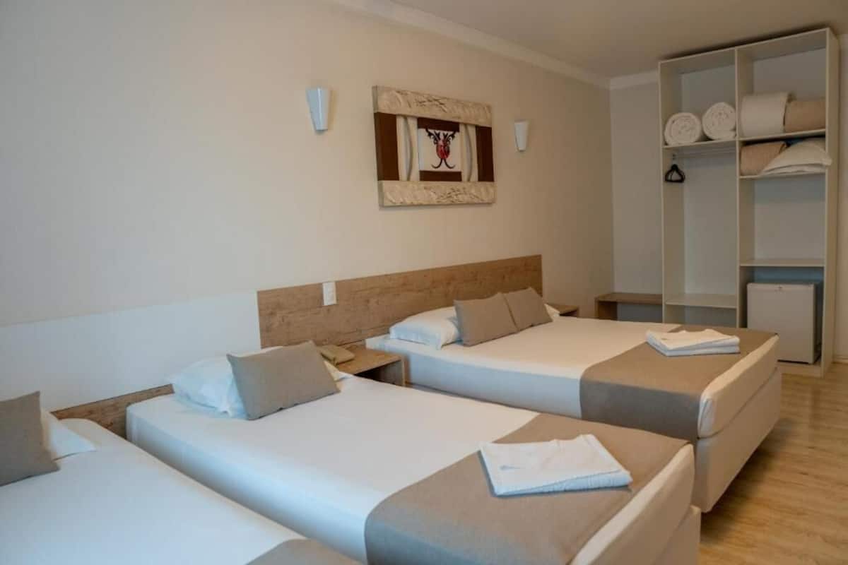 A hotel room with three single beds, a wooden headboard, a wall-mounted artwork, and a built-in wardrobe with shelves.