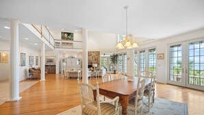 A spacious living area with a wooden dining table, white chairs, and a large window offering a view of the outdoors. - Ocean View, Golf Cart Included, Club Cards Available - 8 River Club (Fripp Island)