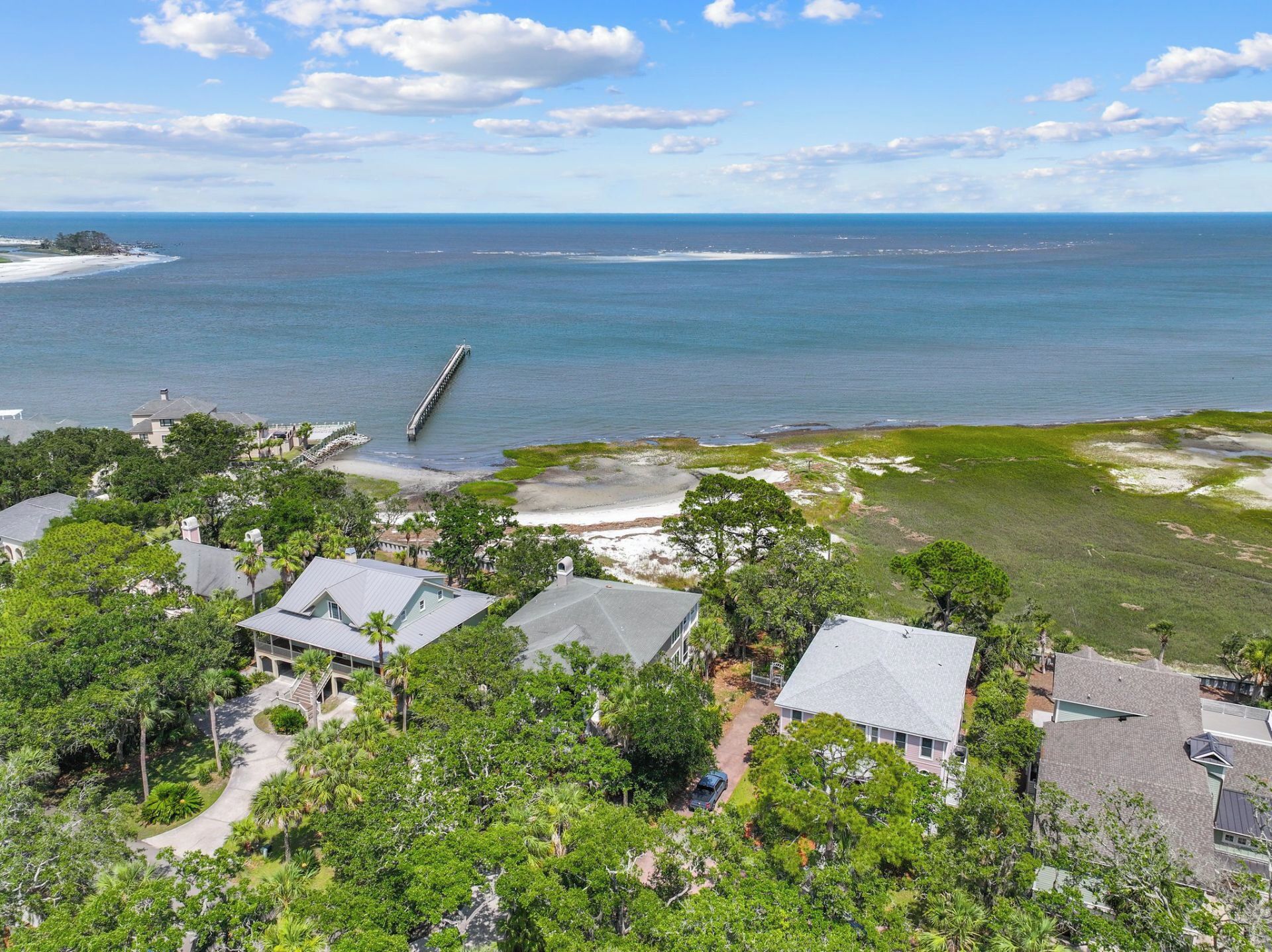 A coastal property with a pier extending into the sea, surrounded by lush greenery and residential buildings.
