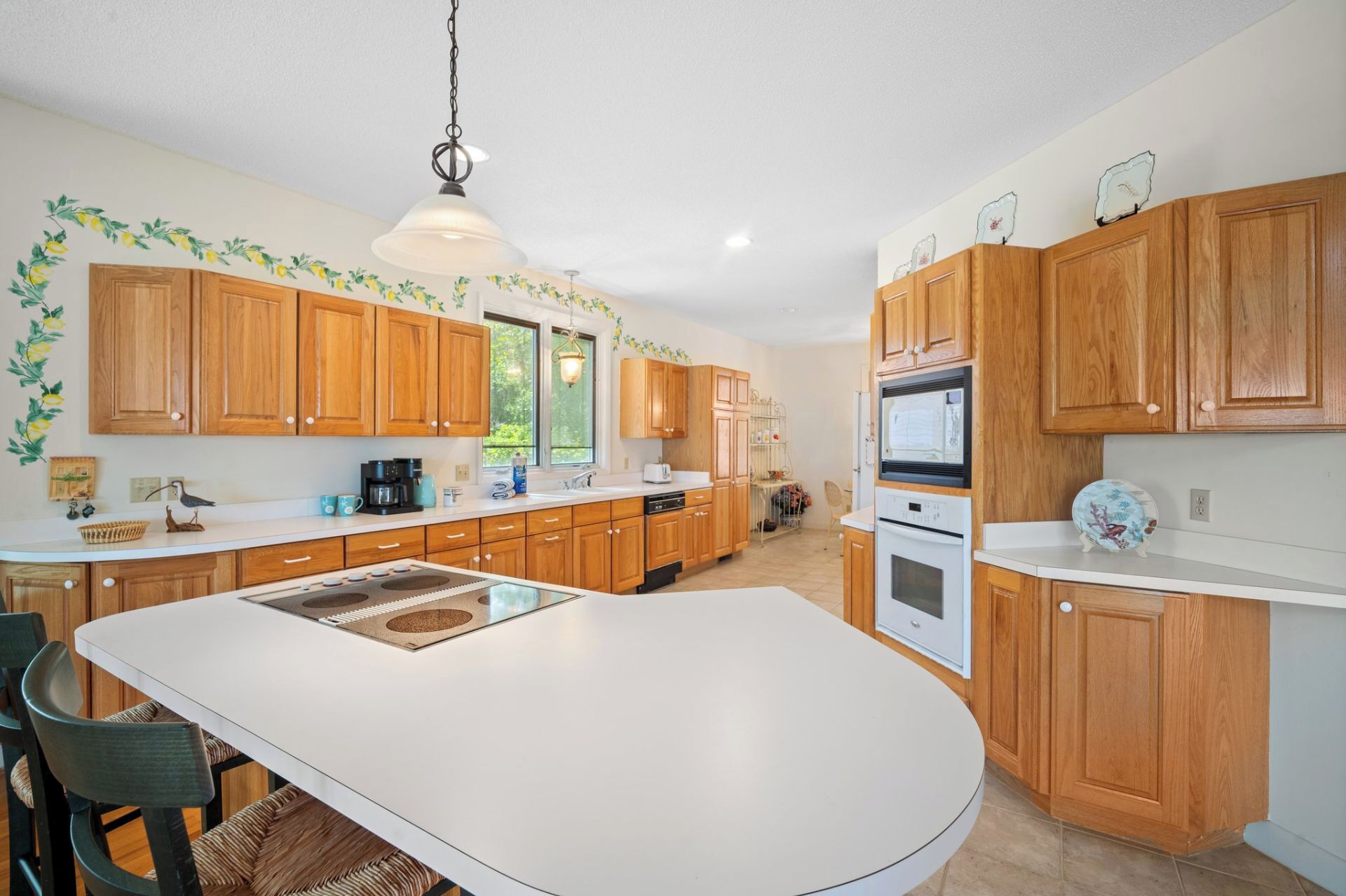 A kitchen with wooden cabinets, a white countertop, a central island, and a hanging light fixture.