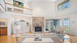 A spacious living room with a stone fireplace, a high ceiling, and a view of the outdoors through large windows. - Ocean View, Golf Cart Included, Club Cards Available - 8 River Club (Fripp Island)