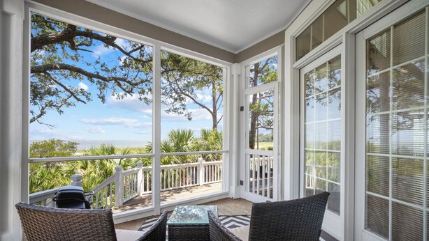 A covered patio with wicker furniture and a glass table, overlooking a scenic view of trees and a body of water. - Ocean View, Golf Cart Included, Club Cards Available - 8 River Club (Fripp Island)