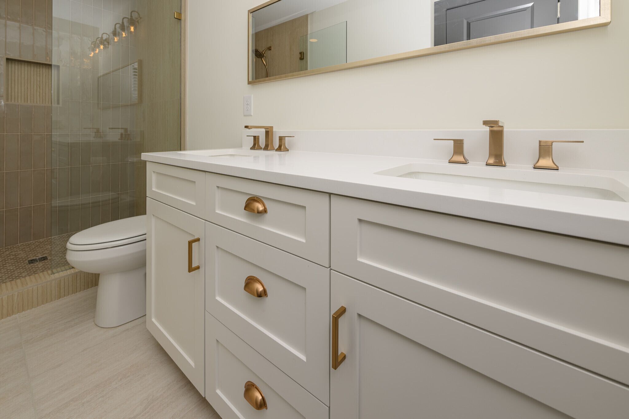 Une salle de bain avec un meuble-lavabo blanc, des robinetteries dorées et une cabine de douche en verre.