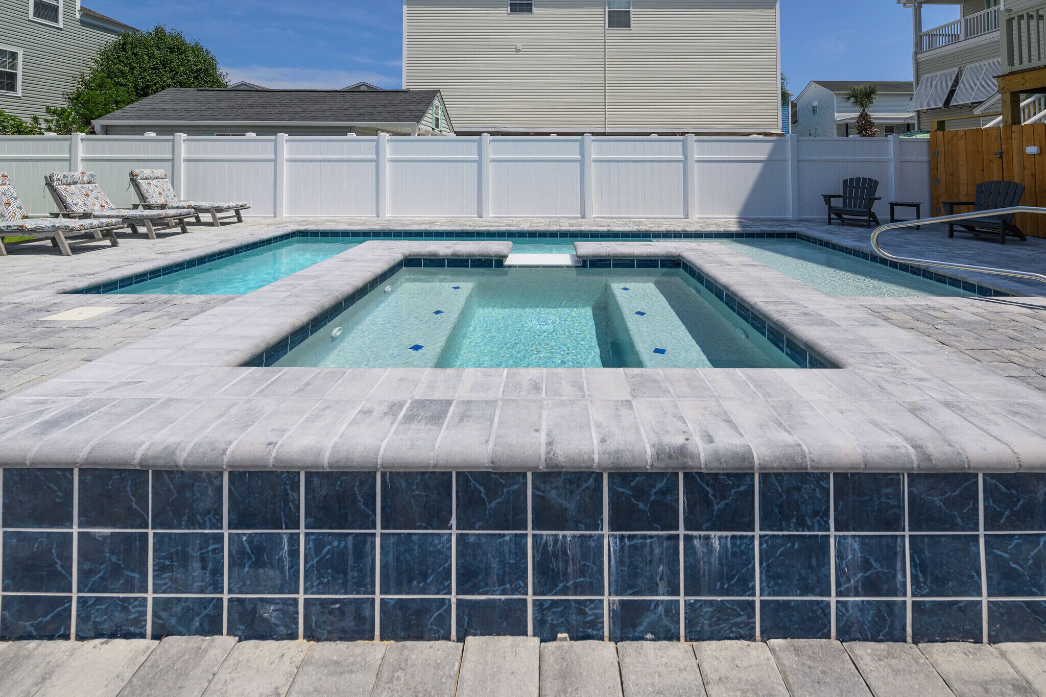 A rectangular pool with a tiled edge, surrounded by lounge chairs and a wooden deck.