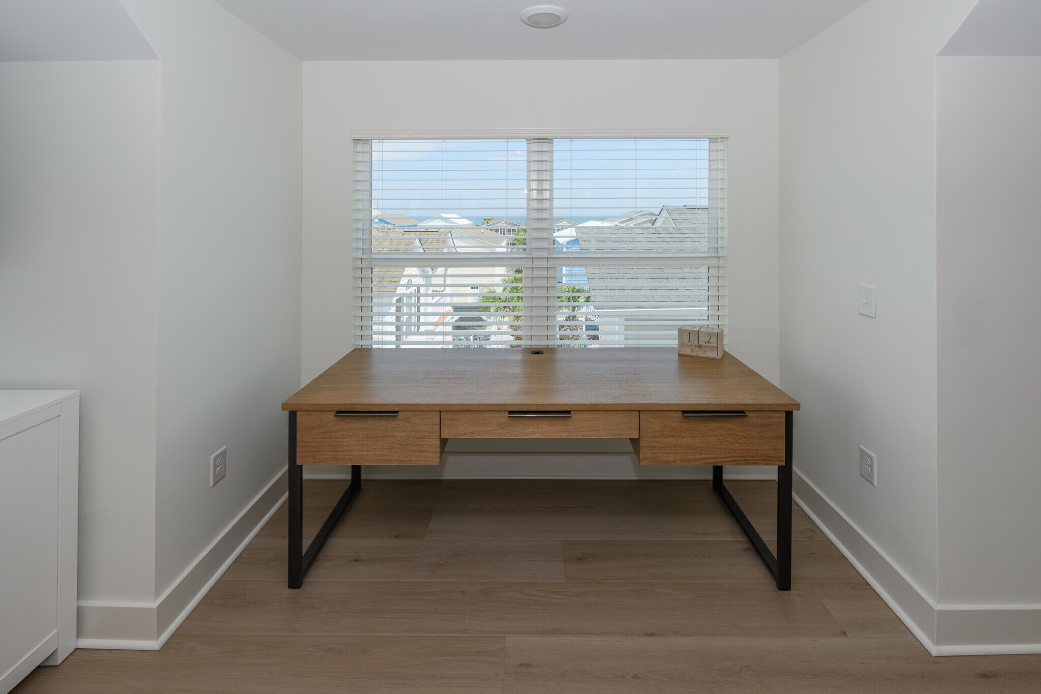 A room with a wooden desk, white walls, and a window with blinds.