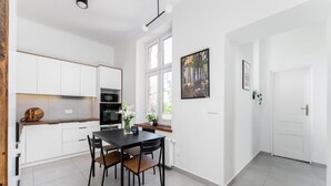 Une cuisine moderne avec des meubles blancs, une table à manger avec des chaises et une fenêtre donnant sur des immeubles.