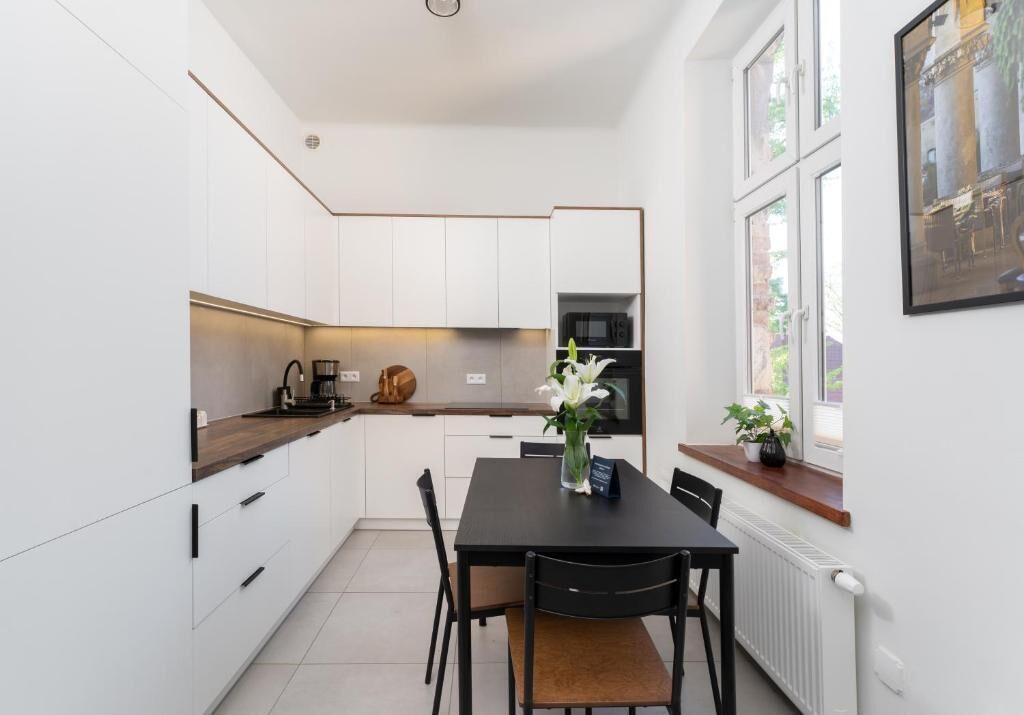 A modern kitchen with white cabinetry, a black dining table, and a window with a view of greenery.