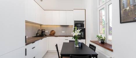 A modern kitchen with white cabinetry, a black dining table, and a window with a view of greenery.