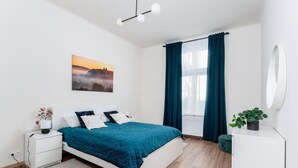 Une chambre moderne avec un lit, des tables de chevet, une commode, une fenêtre avec des rideaux, un miroir fixé au mur et un tableau.