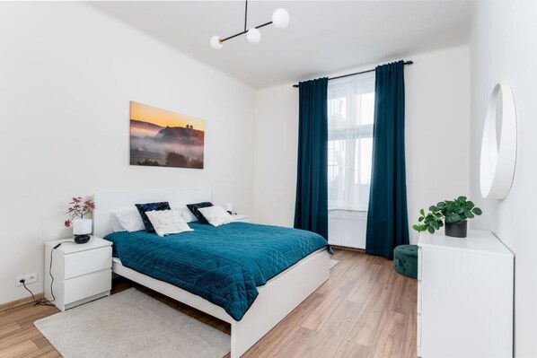 Ein modernes Schlafzimmer mit Bett, Nachttischen, Fenster mit Vorhängen, einem Wandspiegel und einem Gemälde.