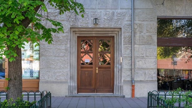 Une entrée d’immeuble avec une porte double en bois, une façade en pierre et une clôture en métal.
