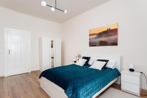 Ein Schlafzimmer mit einem Bett, weißen Nachttischen, einer weißen Tür und einem an der Wand hängenden Gemälde.