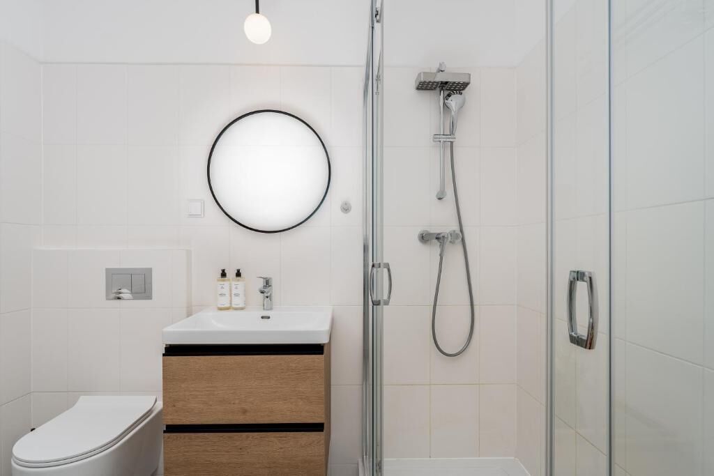 Ein modernes Badezimmer mit Toilette, Waschbecken mit Pflegeprodukten, Dusche mit Handbrause und einer Duschkabine aus Glas.