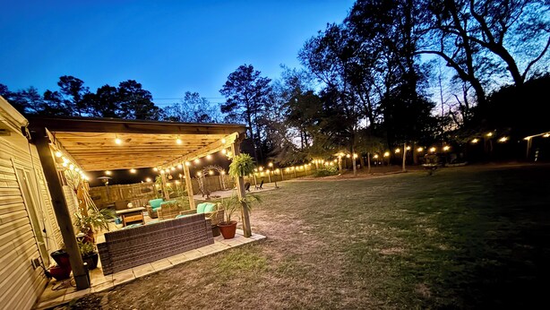 Un espace extérieur aménagé en terrasse, doté d’un coin salon couvert, de guirlandes lumineuses et de plantes en pot.