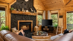 Ein Holzblockhaus-Interieur mit Kamin aus Stein, Ledersofa und einem aufgehängten Hirschkopf.