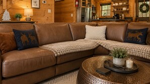 Ein gemütliches Blockhaus-Interieur mit einer braunen Ledersofa, einem runden Couchtisch, Holzwänden, einer Küchenzeile und einer Treppe.