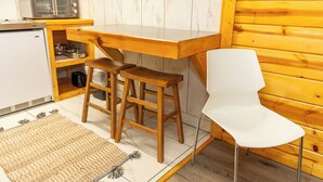 Une cuisine compacte équipée d’un four à micro-ondes, d’un grille-pain et d’un petit réfrigérateur. On y trouve deux tabourets en bois et une chaise blanche.