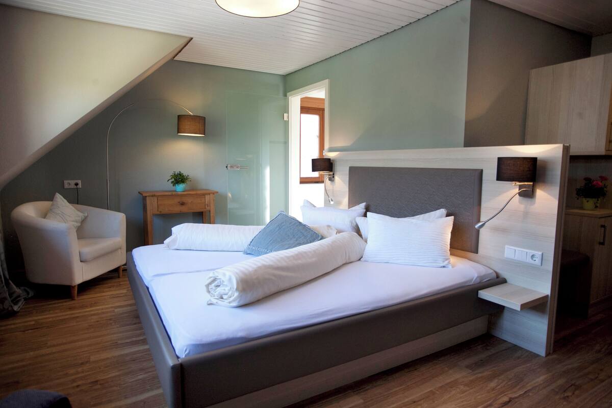 A modern bedroom with a large bed, a small bedside table, a chair, and a desk.