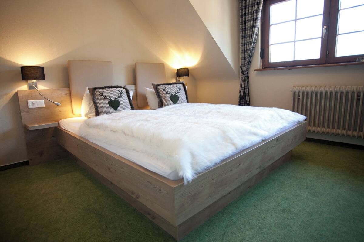 A bedroom with a wooden bed, two bedside tables with lamps, a radiator, and a window with curtains.