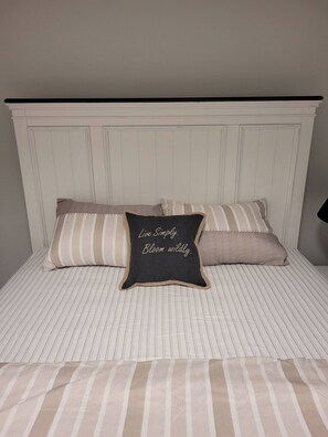 A bed with striped bedding and two pillows, one with a motivational quote. - Luxury One Bedroom Suite in Brighton (Saskatoon)