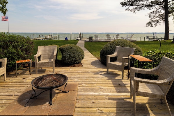A wooden deck with wicker furniture, a fire pit, and a view of the water.