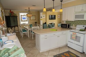 A kitchen with white cabinets, a microwave, an oven, and a dining area with a table and chairs.