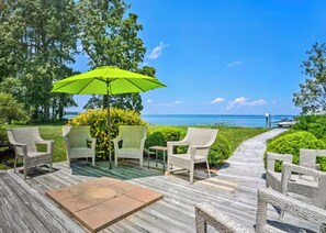 A wooden deck with wicker chairs and a green umbrella, overlooking a clear blue sea. - Lovely 3 BR, Rappahannock Riverfront Retreat in Picturesque Urbanna (Urbanna)