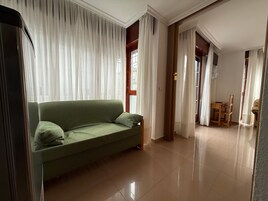 Un salón amplio con un sofá verde, una mesa de comedor de madera con sillas y un gran ventanal con cortinas translúcidas.