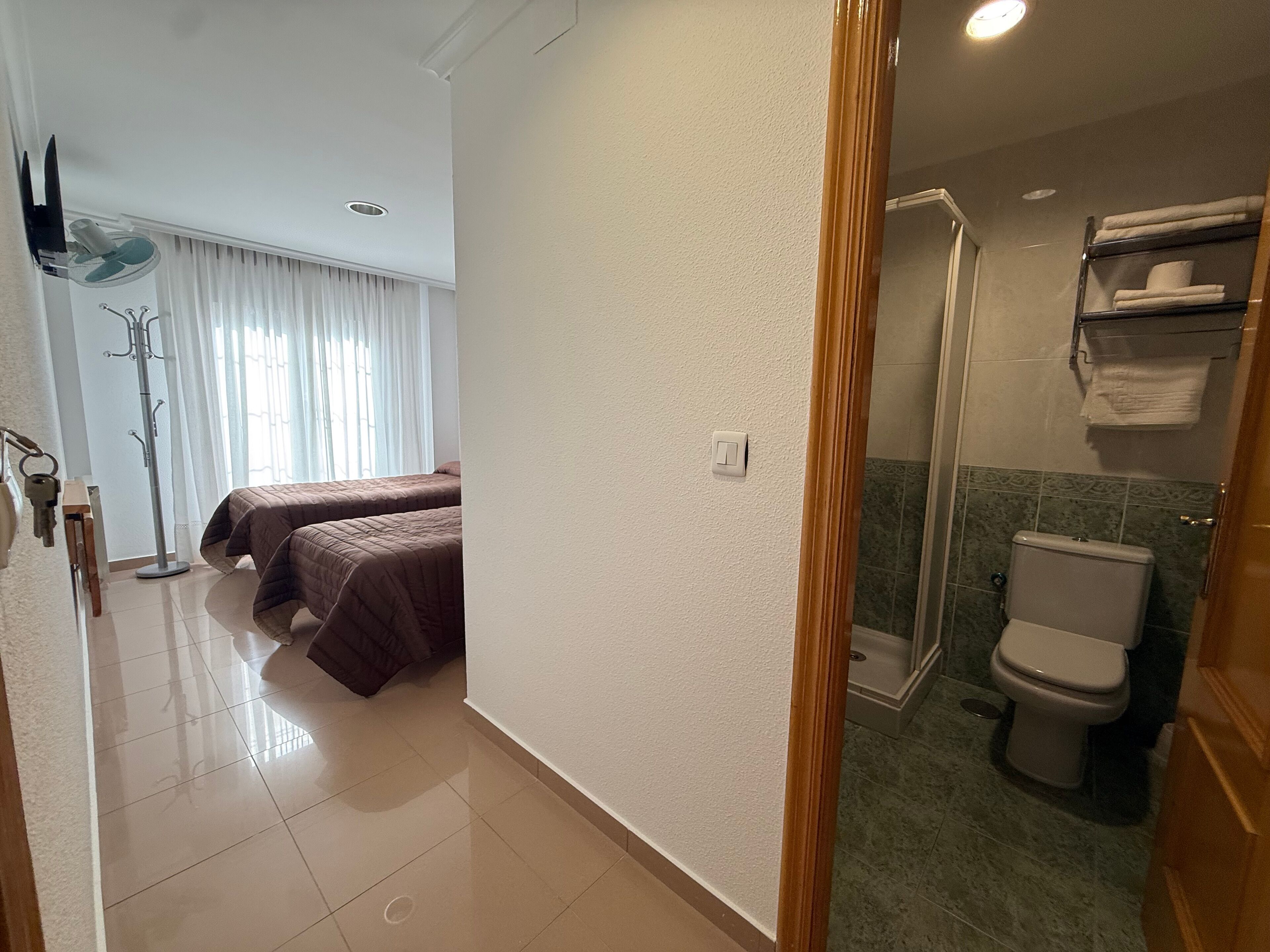 Een hotelkamer met twee bedden, een badkamer met toilet en douche, en een kapstok met sleutels.