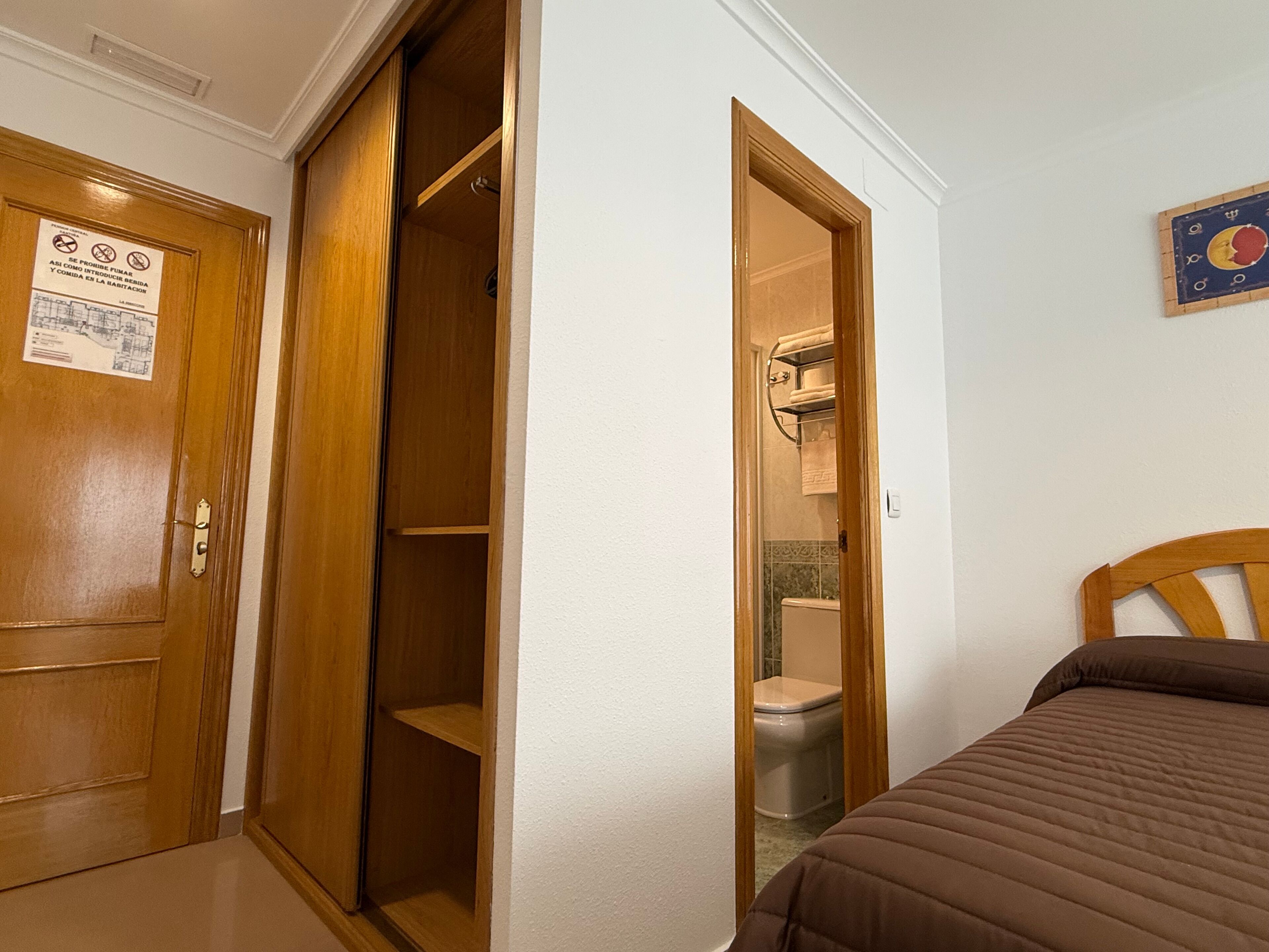 A bedroom with a wooden door, a closet, a toilet, and a bed.