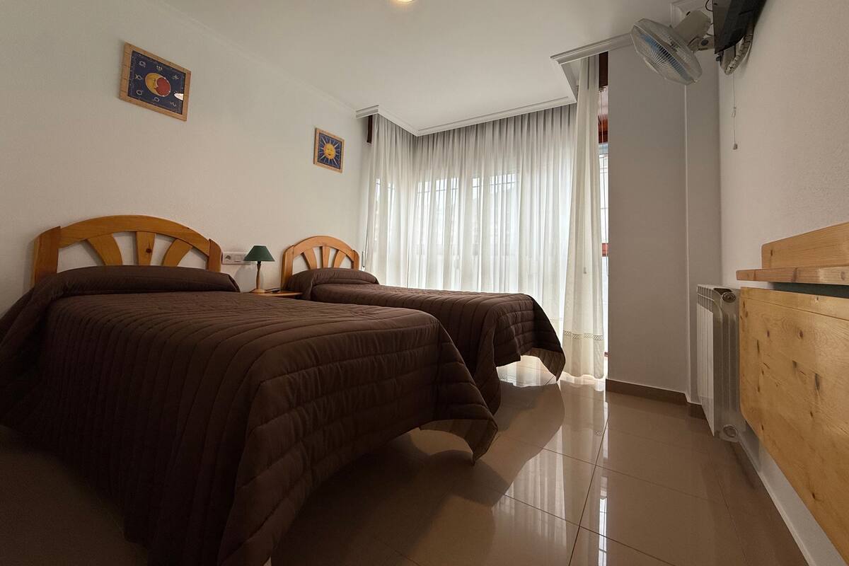 A hotel room with two beds, a TV, a desk, a lamp, and a window with curtains.