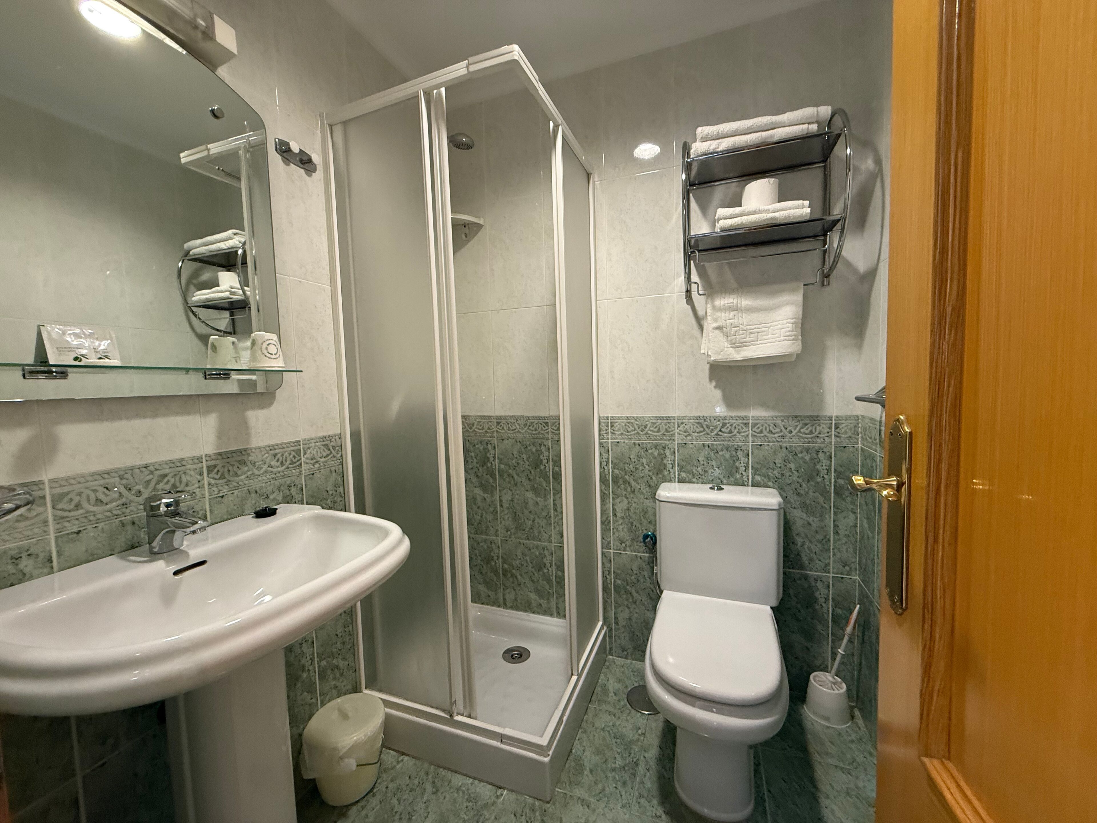 A bathroom with a glass-enclosed shower, a sink, a toilet, and a shelf with towels.