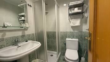 A bathroom with a glass-enclosed shower, a sink, a toilet, and a shelf with towels.
