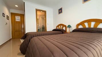 Ein Hotelzimmer mit zwei Betten, einer Holztür, einem Duschbereich und einem kleinen Tisch mit einer Lampe.