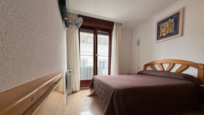 Une chambre à coucher avec une tête de lit en bois, un lit recouvert d’une couverture marron, un radiateur, une fenêtre avec des rideaux et un tableau accroché au mur.